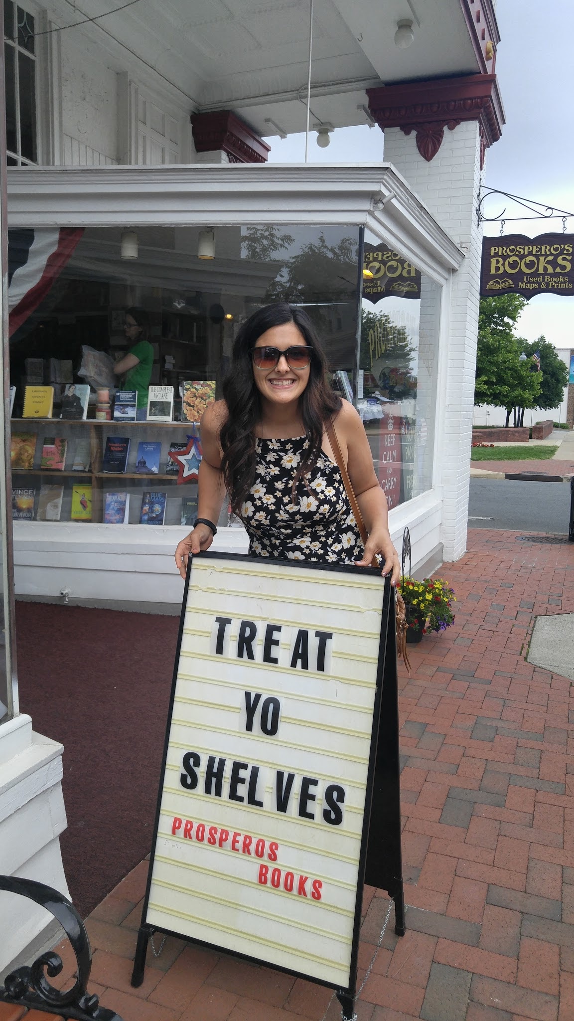 Jen in front of a bookstore with a sign that reads, "Treat your shelves"